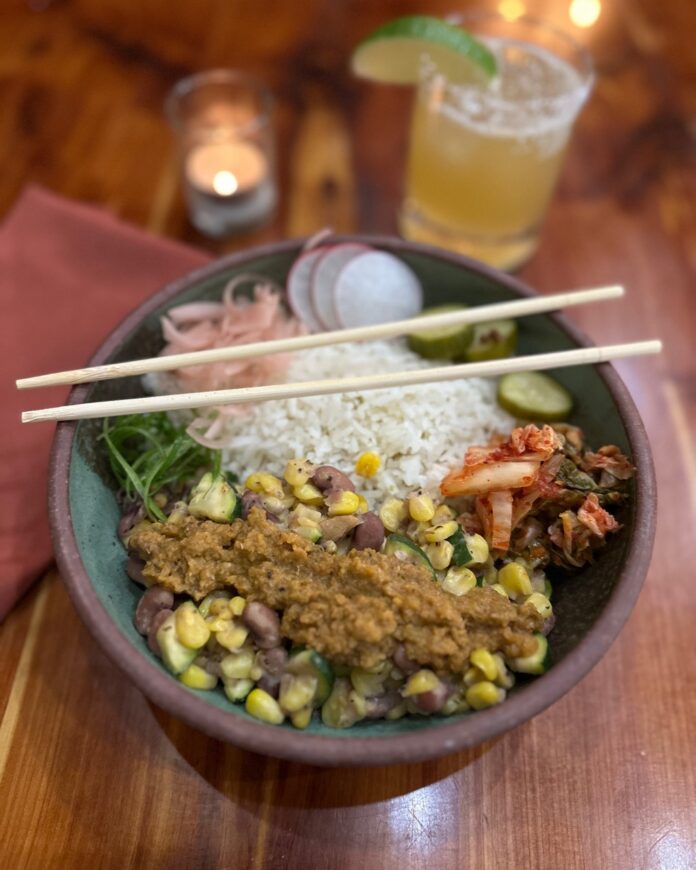 A bowl full of grains, vegetables, and rice with chopsticks laying overtop.