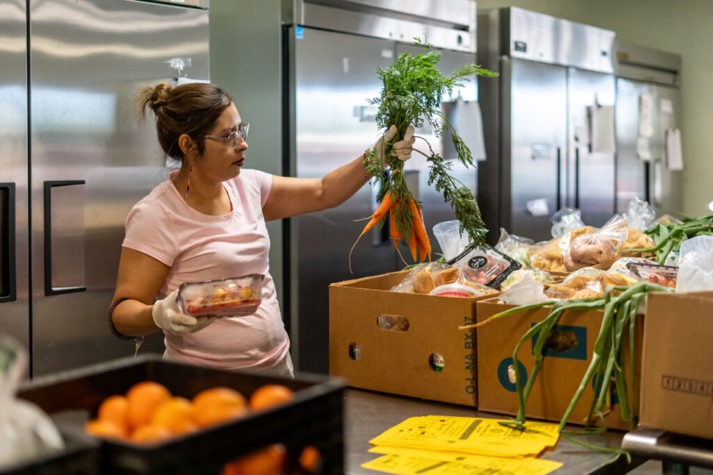 A woman holds up carrots out of a produce box.