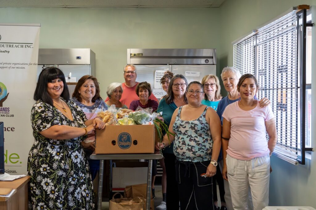 A group of food depot volunteers gather around boxes of produce.