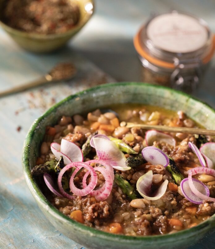A bowl of Bolita Bean and Fennel Sausage Soup sits on a table.