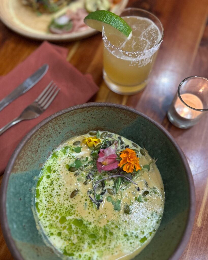 A green bowl full of butternut squash green soup below a margarita with a lime on the rim.