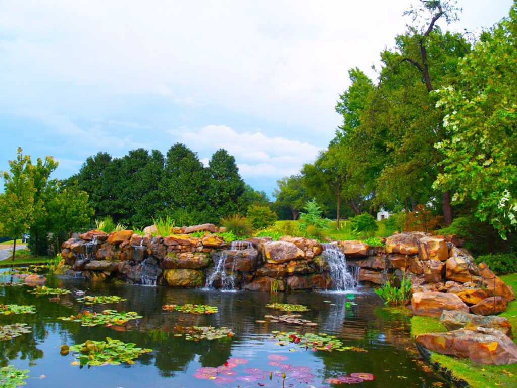 A pond with small waterfalls and lily pads around greenery.
