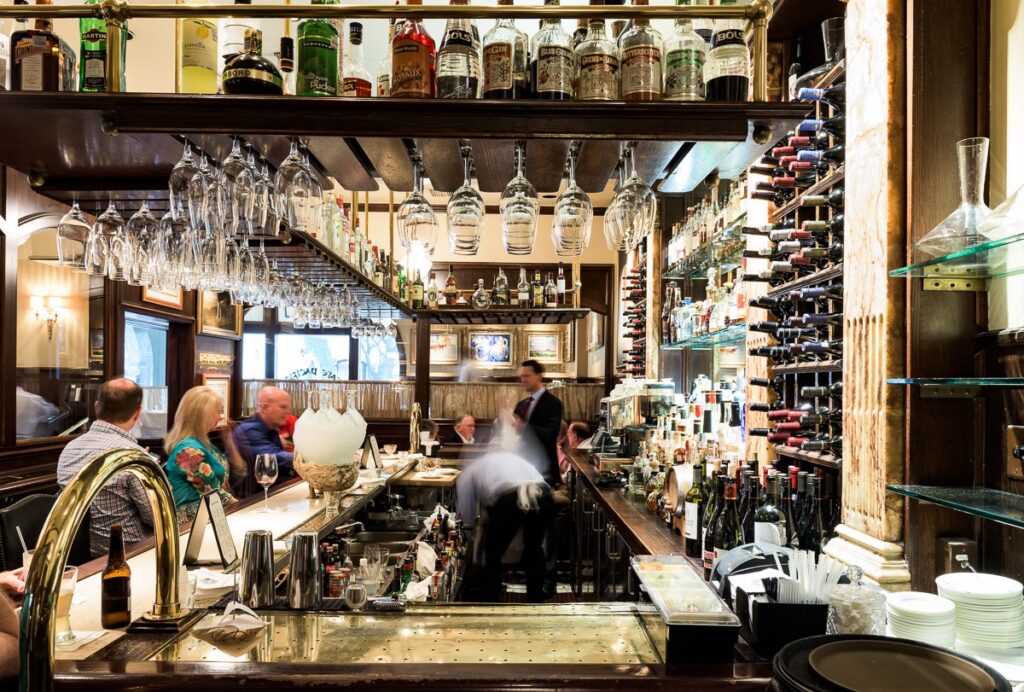 Two bartenders work behind a bar full of cocktail glasses.
