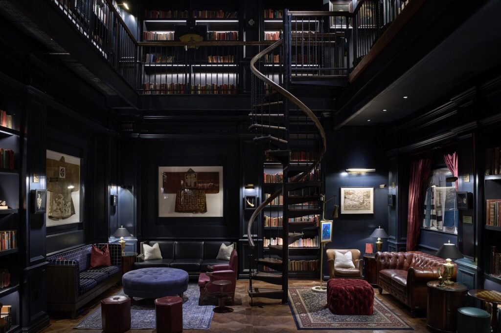 The inside of The Library at Hotel Swexan with tall dark shelves into a second floor and a spiral staircase in the center.