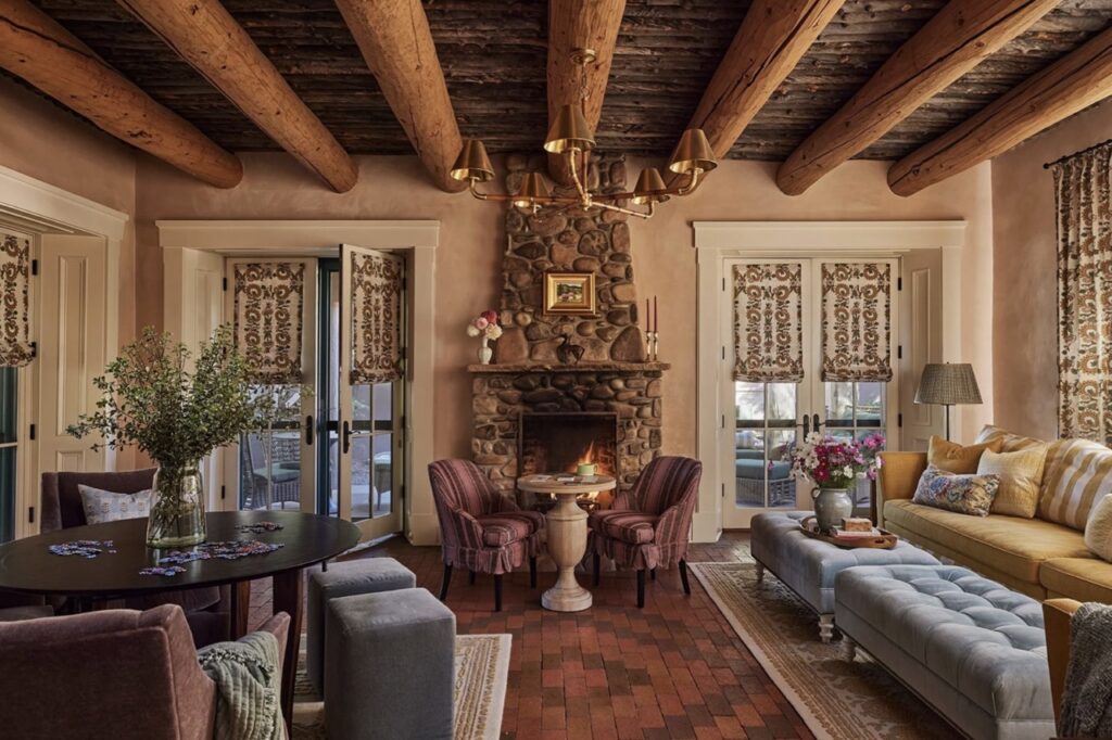 A den space with wood beams, a stone fireplace, and cozy furniture.