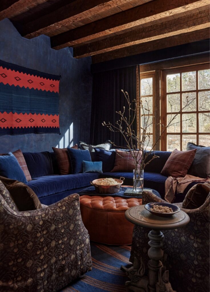 A blue and red accent living room with dark walls and long couches in front of a window.