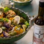 A green bowl with cauliflower and various veggies beside a bottle of lemony olive oil.