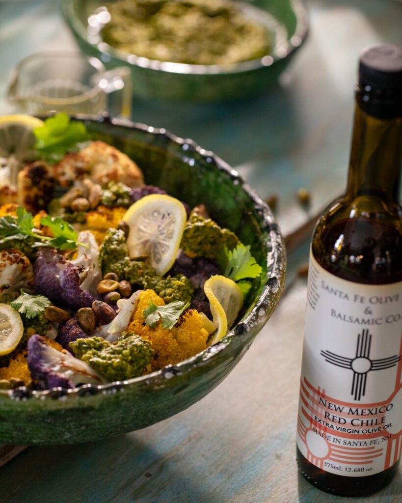 A green bowl with cauliflower and various veggies beside a bottle of lemony olive oil.