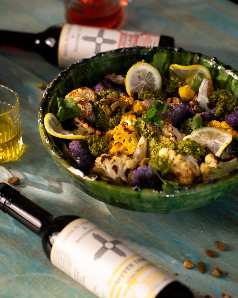 A green bowl of cauliflower and lemon slices with two bottles of olive oil laying on the table.