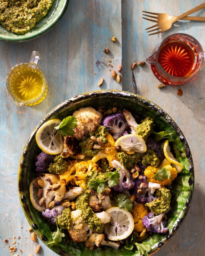 Cauliflower tossed with lemon slices in a green bowl with two colored olive oils above it.