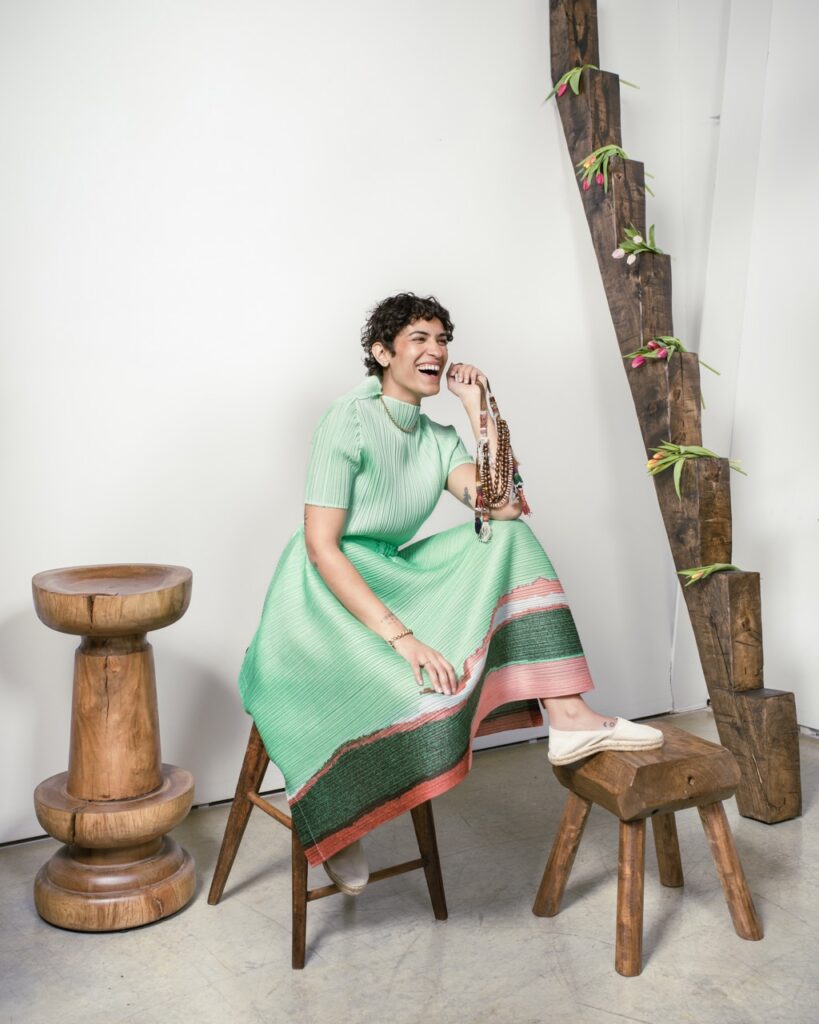 A woman in a light green dress sits on a stool and puts her feet up on another.