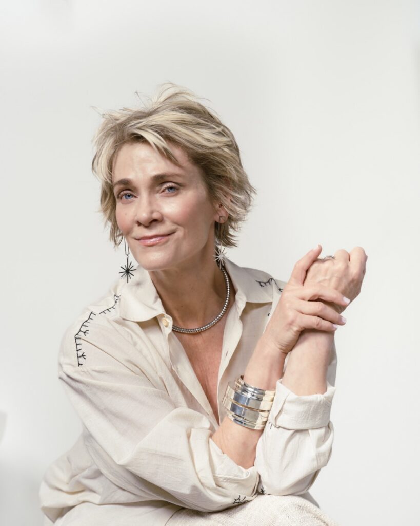 A woman sits with her hands on her knees in a white blouse.