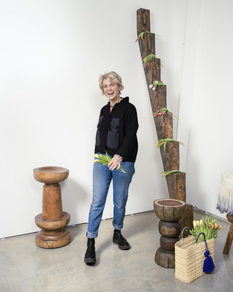 A woman in a black shirt and jeans stands in a white studio.