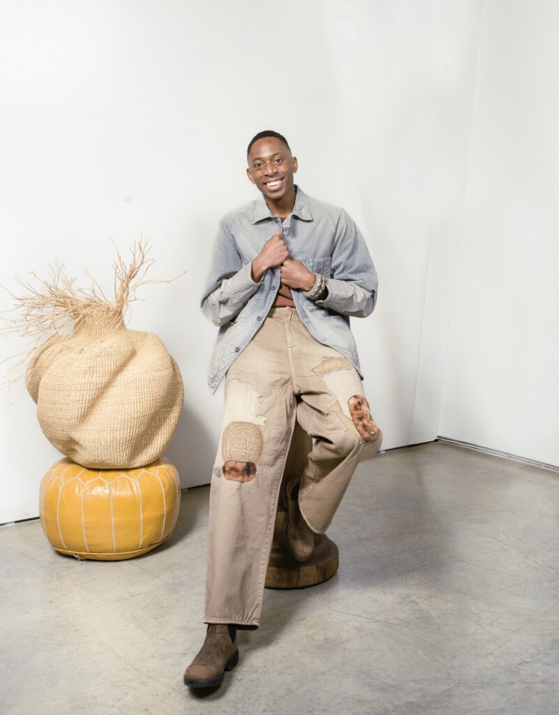 A man sits in a grey suit jacket and brown pants.