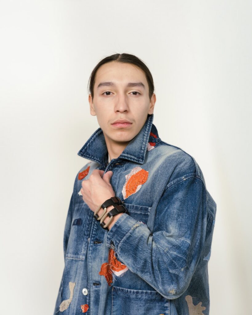 A man stands in a jean jacket with the collar up.
