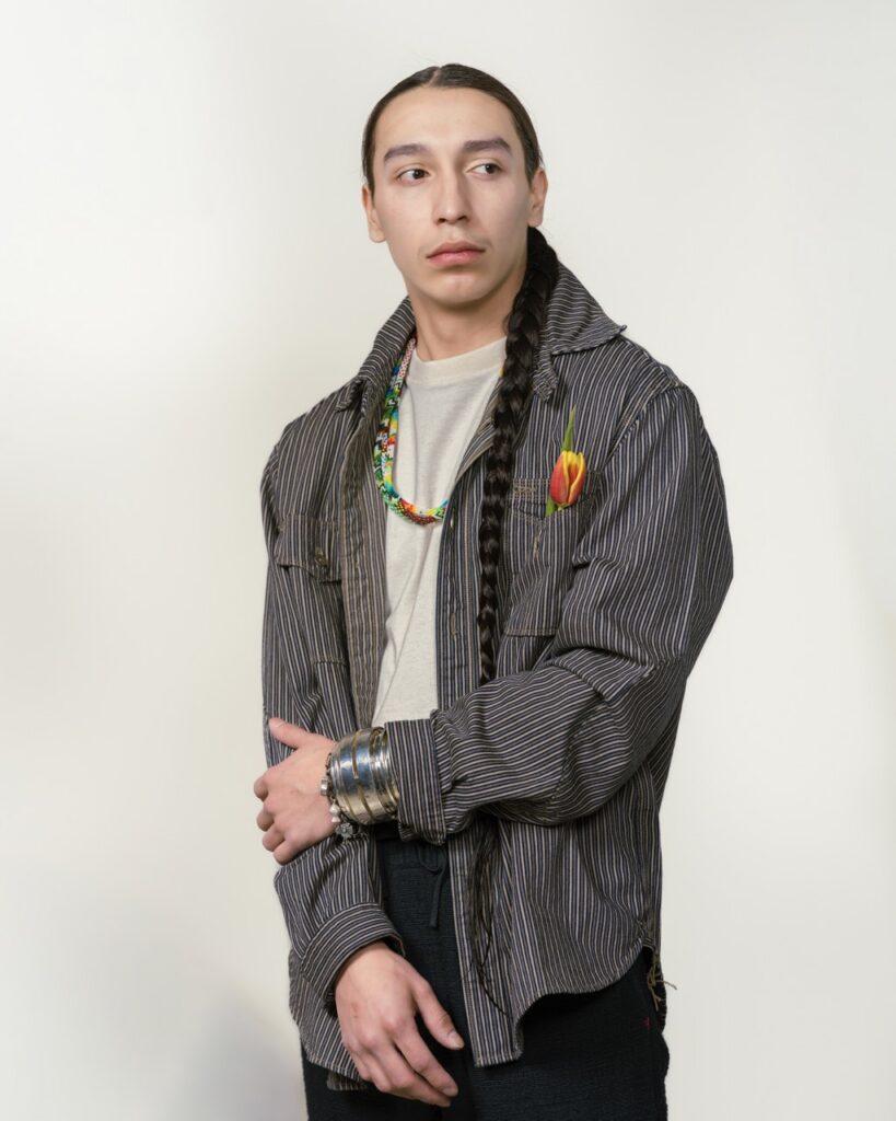 A man stands in a black jacket with a white shirt.