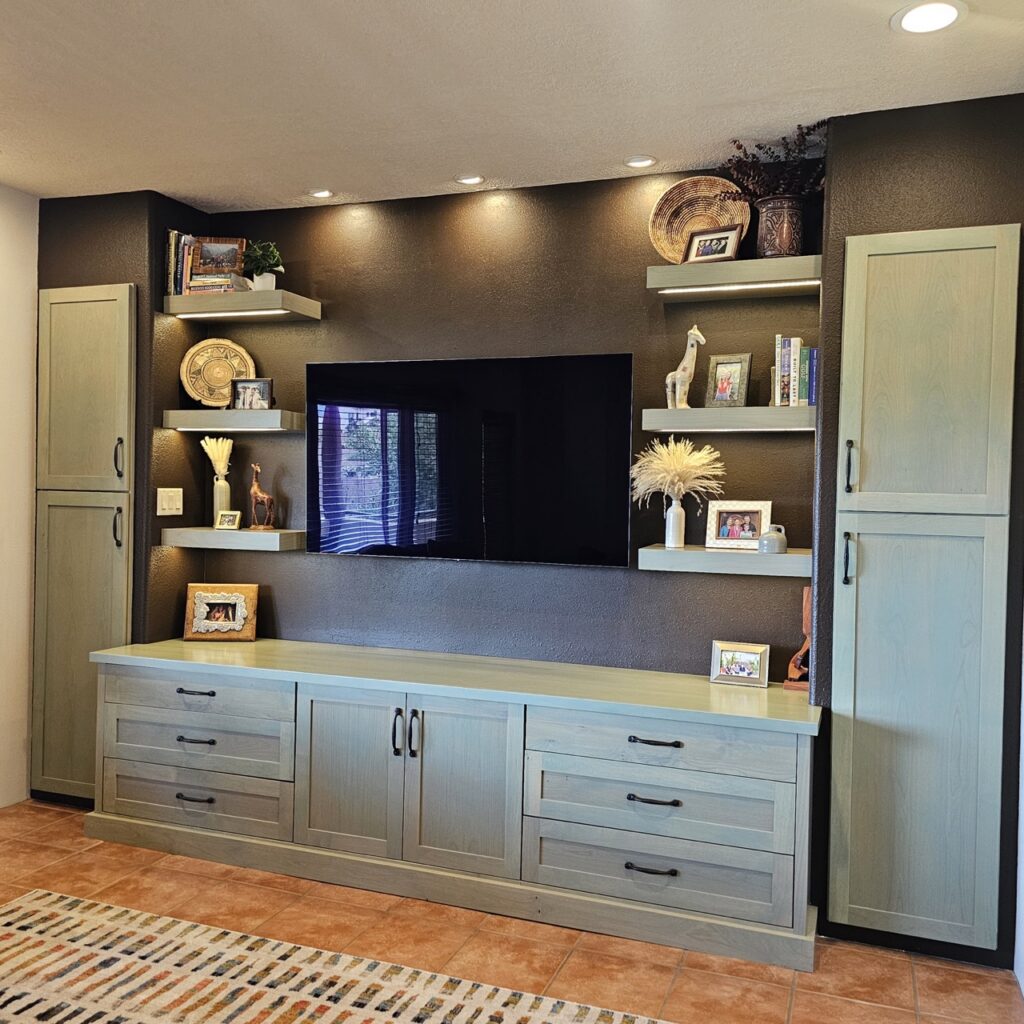 Sage cabinets against a dark wall with shelves around a TV in the center.