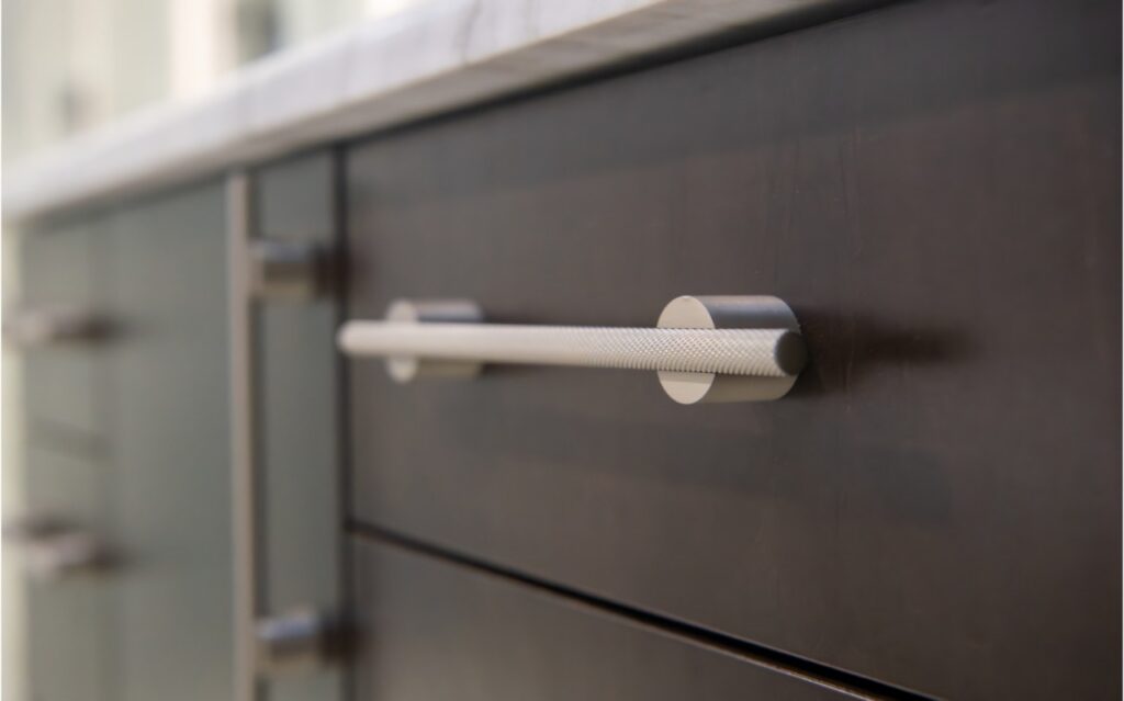 Up close of a metal drawer handle on a black cabinet.