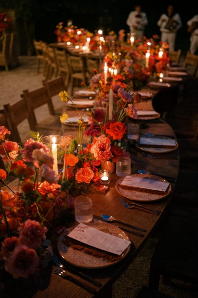 A candlelit outdoor wedding reception table at Villa Santa Cruz in Todos Santos, Mexico, featuring vibrant floral centerpieces and a Mariachi band in the background.