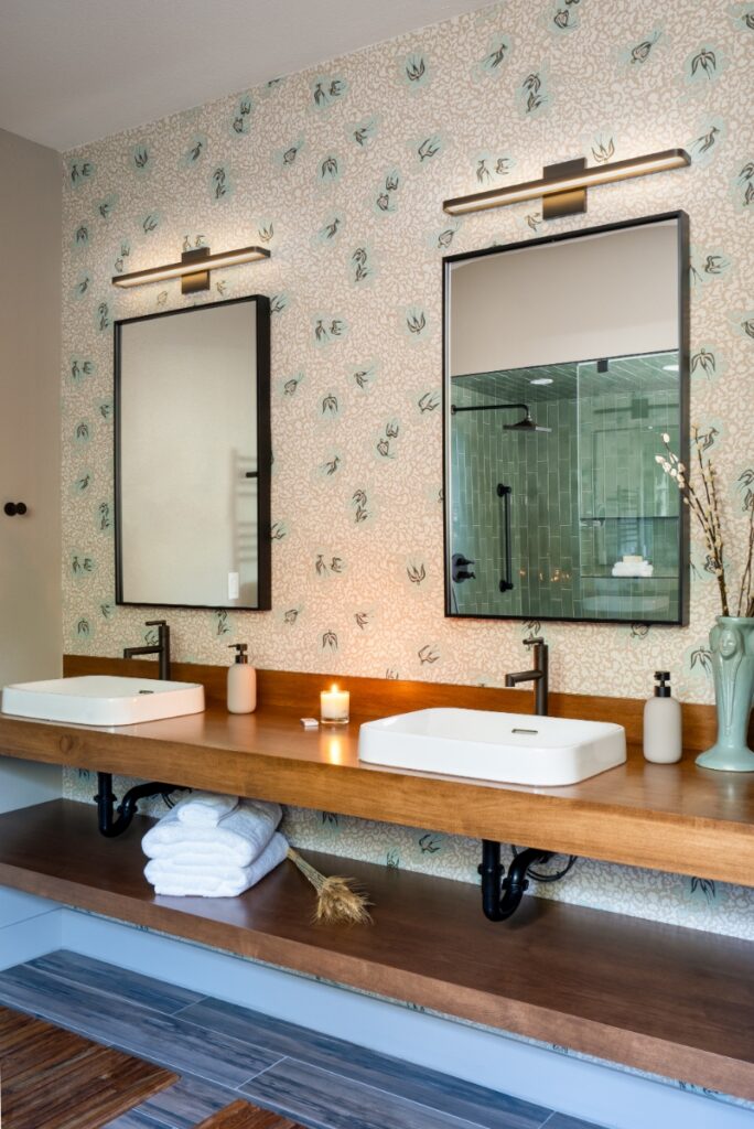 A double bathroom vanity featuring custom wood floating shelves by El Tapanco Woodcrafts, modern white vessel sinks, and patterned wallpaper, designed by Three Roots Design.