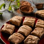 Nine extra dark brownies topped with a swirl of coffee mascarpone frosting and a dusting of cocoa powder, arranged on a red ceramic plate for dessert.