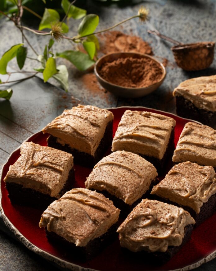 Nine extra dark brownies topped with a swirl of coffee mascarpone frosting and a dusting of cocoa powder, arranged on a red ceramic plate for dessert.