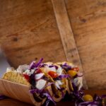 Three fish tacos in hard shells with purple slaw and tomatoes.