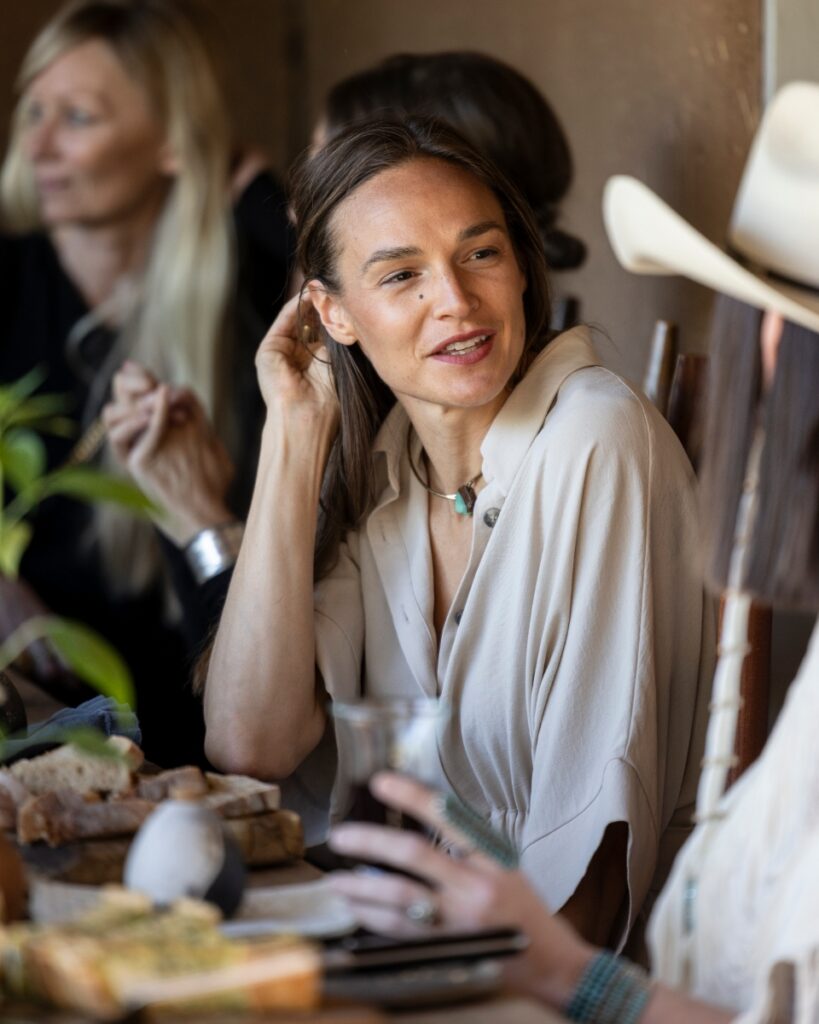 A guest in a tan silk shirt and turquoise necklace engaged in conversation at a Santa Fe dinner party held at a rustic adobe home.