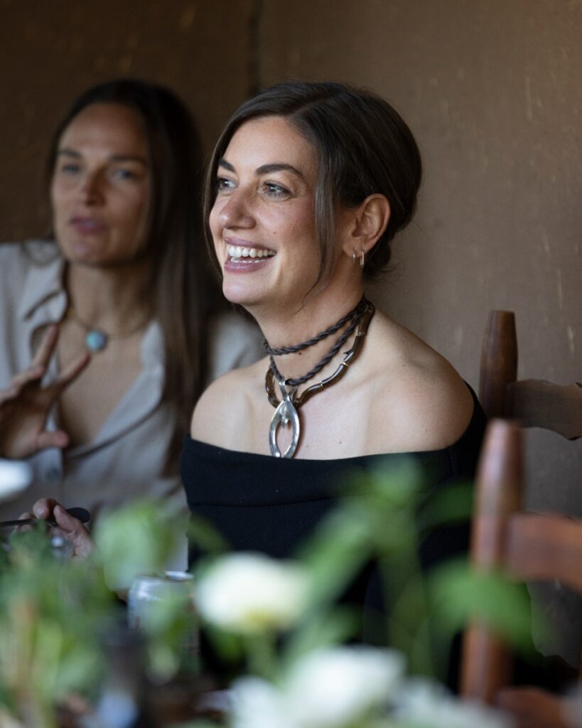 A guest smiling during a lively conversation at Katie Rodgers' house party in Santa Fe, wearing a distinctive silver Naja pendant necklace.