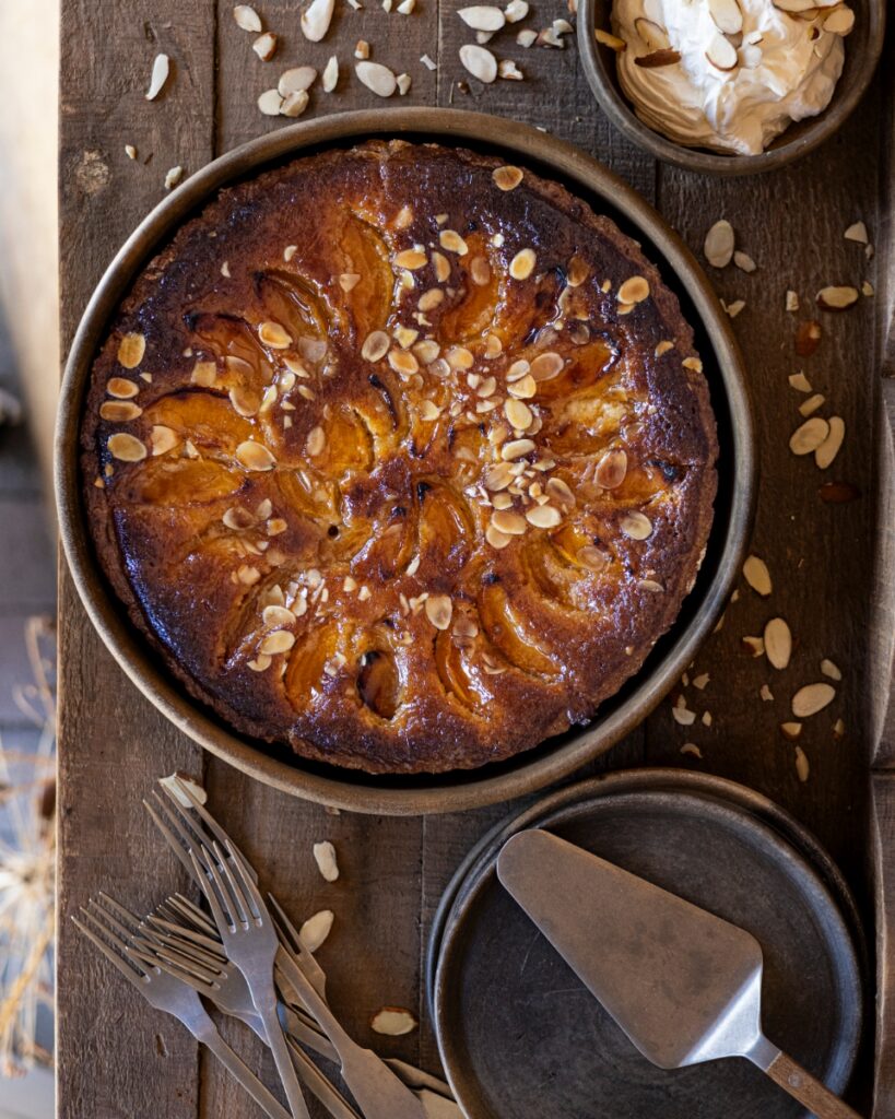 A golden-brown almond apricot tart topped with sliced nuts, served with whipped cream.