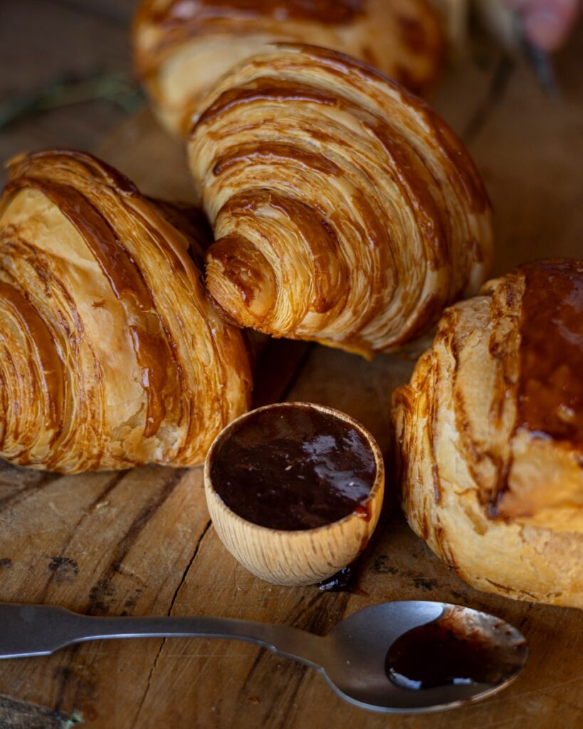 Flaky golden croissants on a wooden board served with a small pot of dark strawberry jam at a brunch in Santa Fe.
