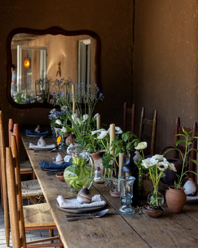 Artist Katie Rodgers hosting a springtime party at her Santa Fe adobe home, featuring a rustic wooden table set for brunch and a crate of vibrant pastels.