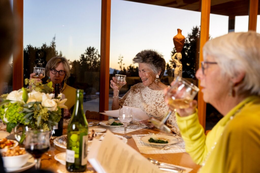 Pat Stanley and guests raising wine glasses for a Passover Seder toast at her home in Santa Fe, with a sunset view of the mountains through the window.