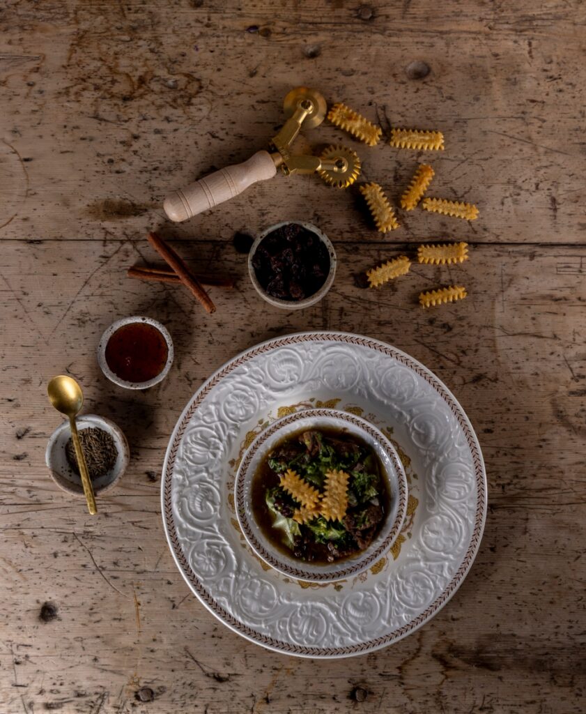 A slow-cooked Sephardic lamb stew seasoned with cumin, cinnamon, honey, and raisins, served on a vintage patterned plate for a Santa Fe Passover Seder.