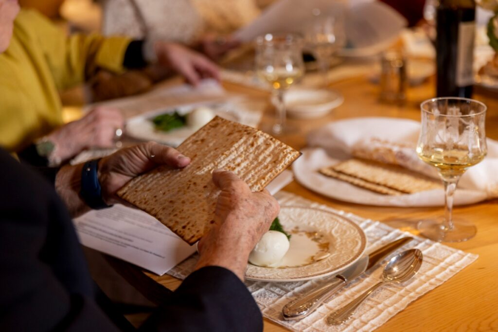A guest holding a piece of handmade matzah during a Passover Seder dinner in Santa Fe, with a traditional Seder plate and wine glass in the background.
