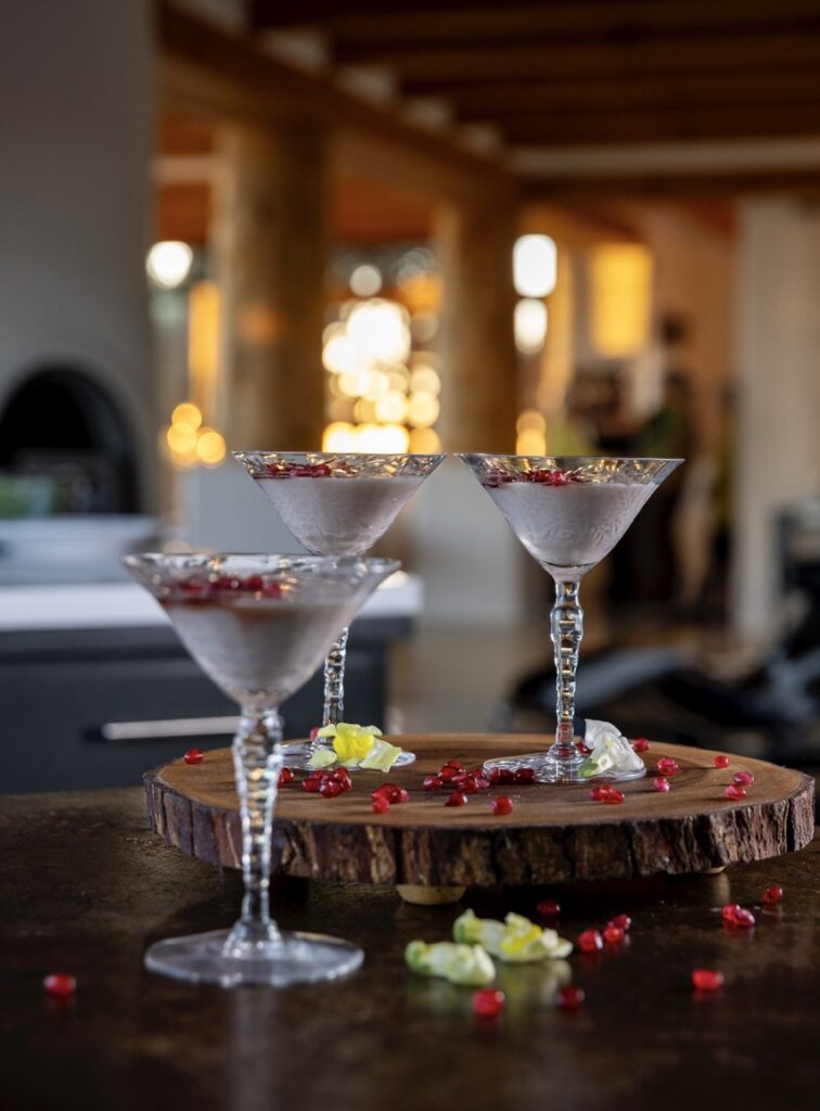 Three cups full of a white pudding with red pomegranate seeds on top.