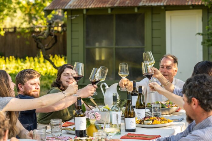 A spring dinner table setting featuring a bottle of Cline Family Cellars Mourvèdre red wine, grilled meats, and fresh seasonal side dishes.