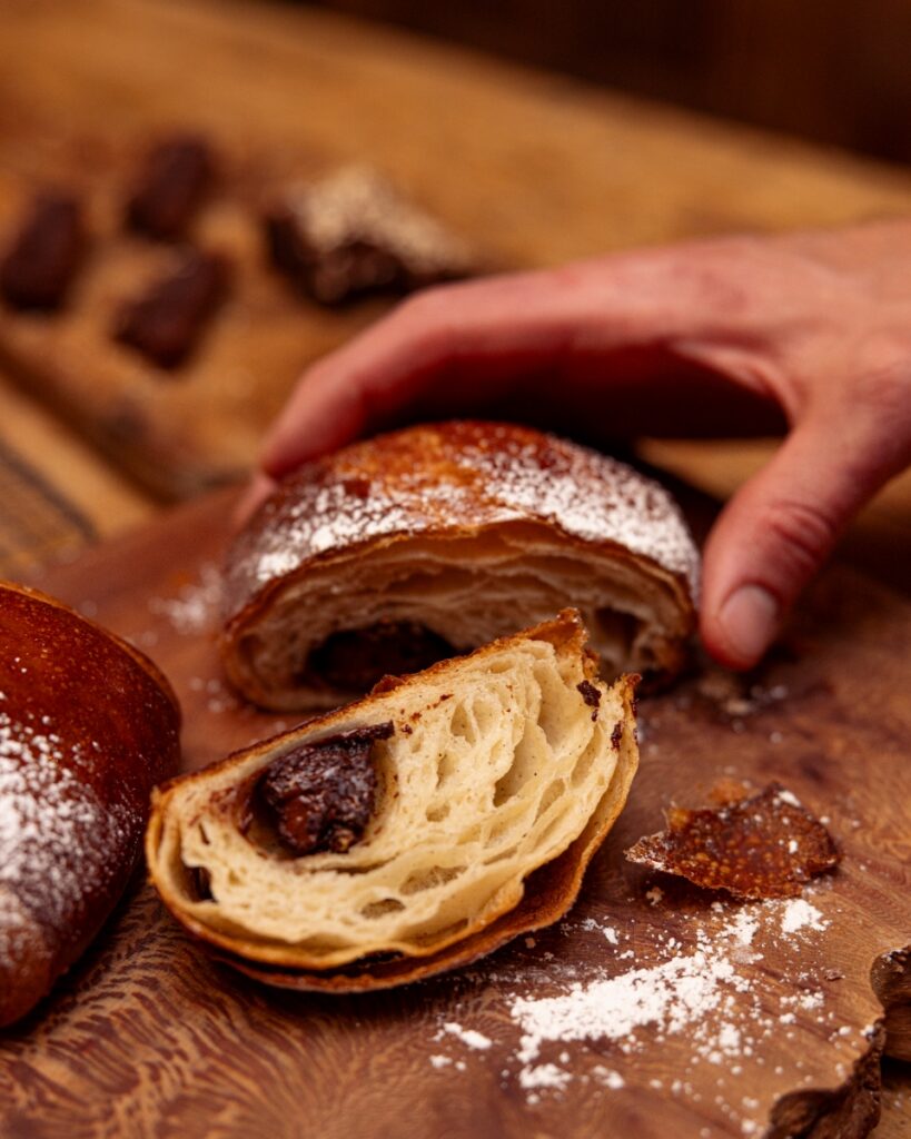 A hand-laminated puff pastry croissant filled with chocolate tahini brownie, sliced to show the buttery layers.