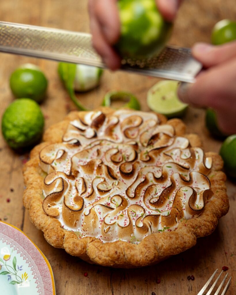 Baker Chase Maus zesting a fresh lime over a toasted meringue pie on a rustic wooden tabletop in Santa Fe.