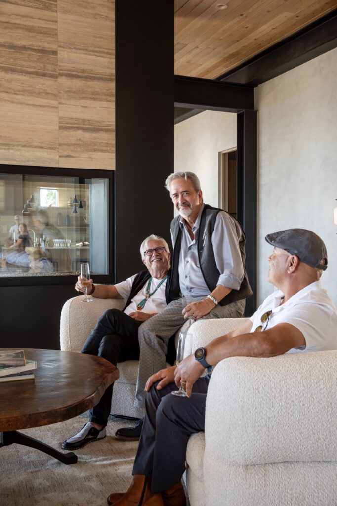 Two men sit in white leather chairs as a third sits on the arm of one of the chairs.