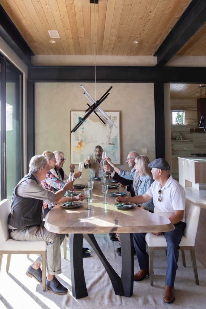 A group of people cheers while sitting at a wood dining table with leather chairs.