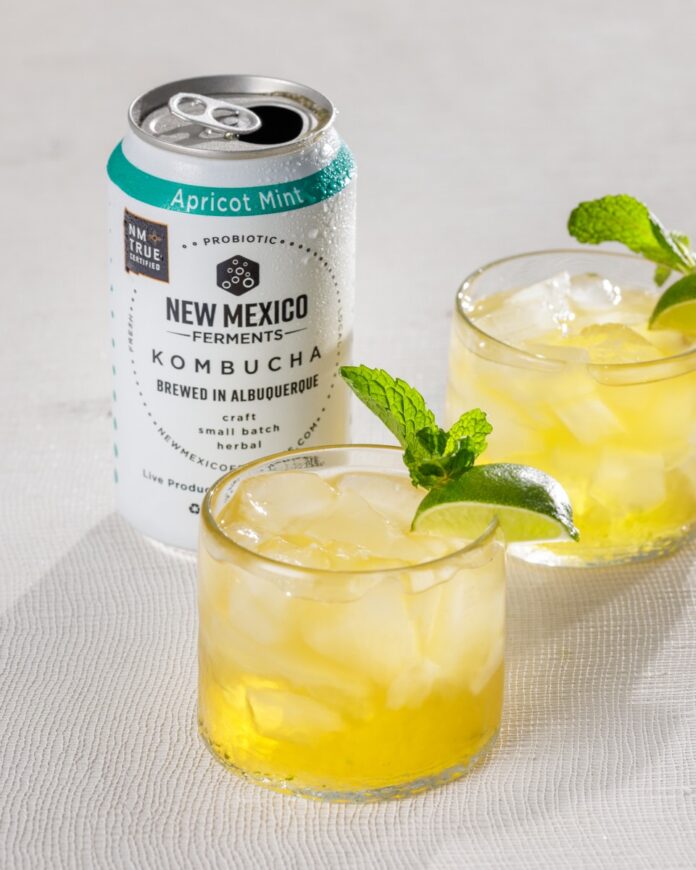 Apricot Mint Mojito TABLE Magazine Two glasses of a yellow cocktail with a sprig of mint sit in front of a can of New Mexico kombucha.