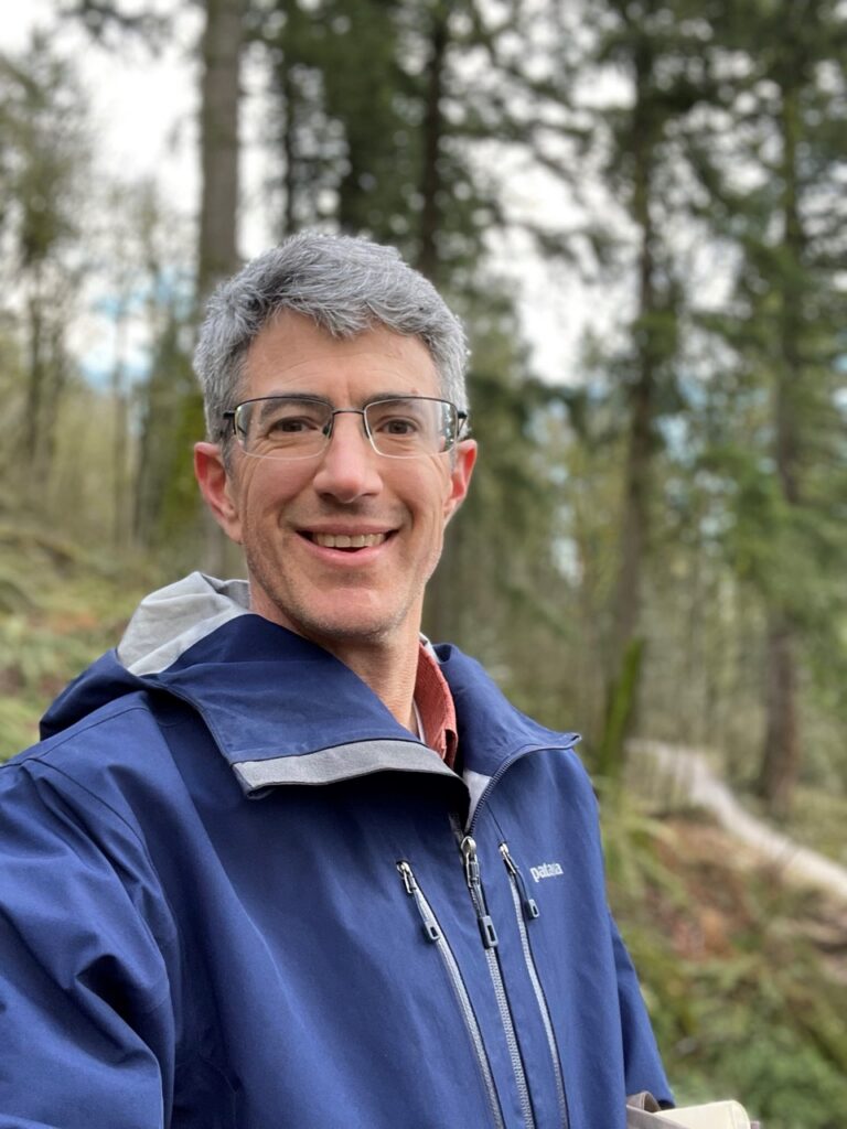 Zander Evans stands in a blue jacket in the forest.