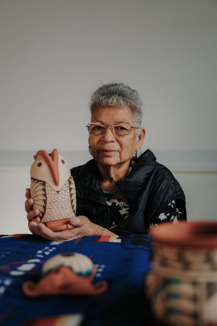 A Native American woman holding a piece of artwork shaped like a fish.