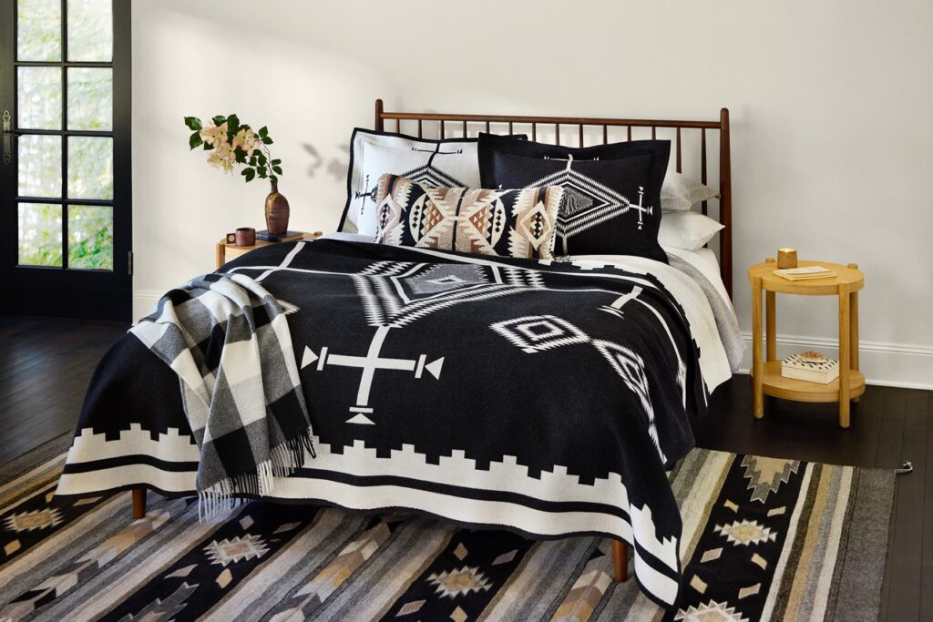 A bed with a black and white pattern comforter on a similar looking carpet and with matching pillows.