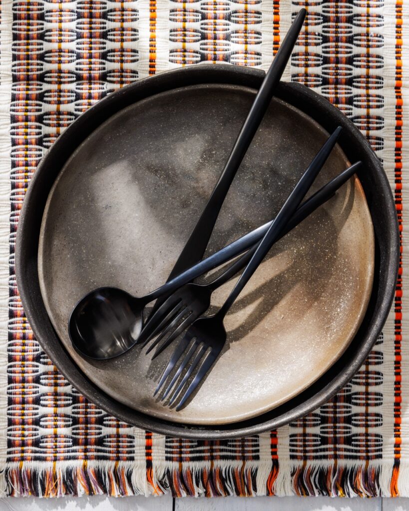 A gray plate with two forks and long spoon on the top of the plate.