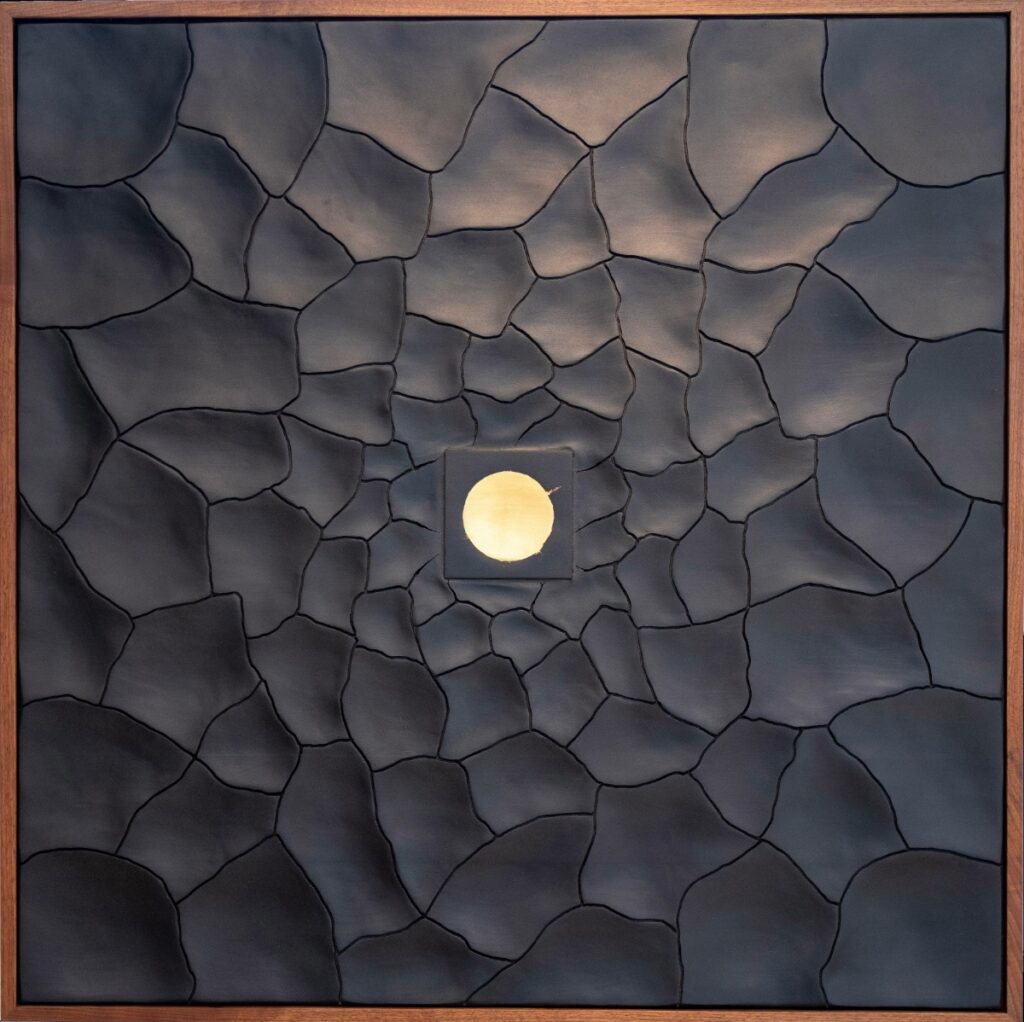 Organic wall sculpture by Jeddadiah Emanuel featuring dark, textured wood pieces arranged in a sunburst pattern around a central gold circle.