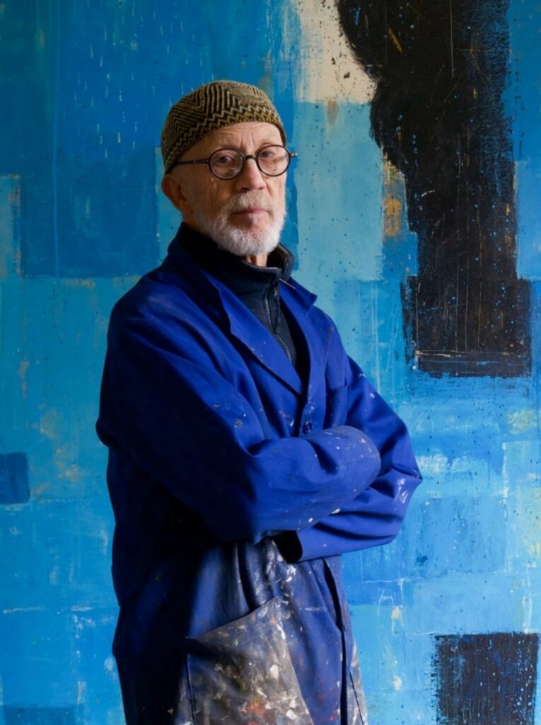Artist Kevin Tolman standing in front of a large-scale blue abstract painting in his studio.