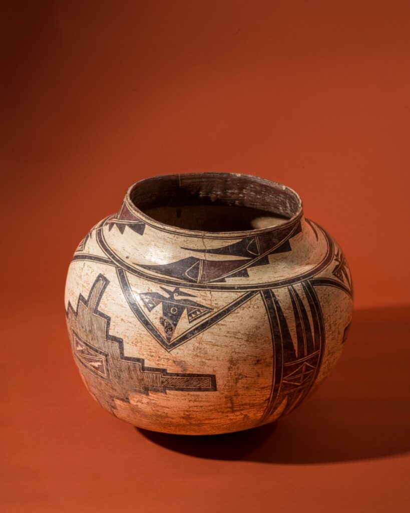 A historic Zuni Pueblo water jar from circa 1850, featuring a traditional bulbous shape with intricate black and red geometric patterns and floral motifs hand-painted on cream-colored clay.