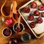 A silver tray of pink grapefruits and plums beside three jars of plum and pink grapefruit jam.